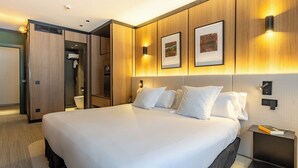 Une chambre d’hôtel avec un grand lit, un dressing, une douche et une table de chevet avec un livre.