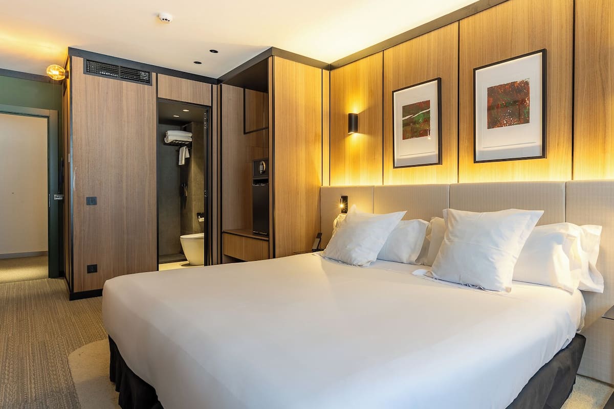 Quarto de hotel com cama grande, closet espaçoso, chuveiro e mesa de cabeceira com um livro.