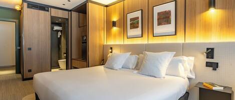 Une chambre d’hôtel avec un grand lit, un dressing, une douche et une table de chevet avec un livre.