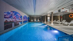 Une piscine intérieure ornée d’une fresque représentant des montagnes et dotée d’un plafond transparent.