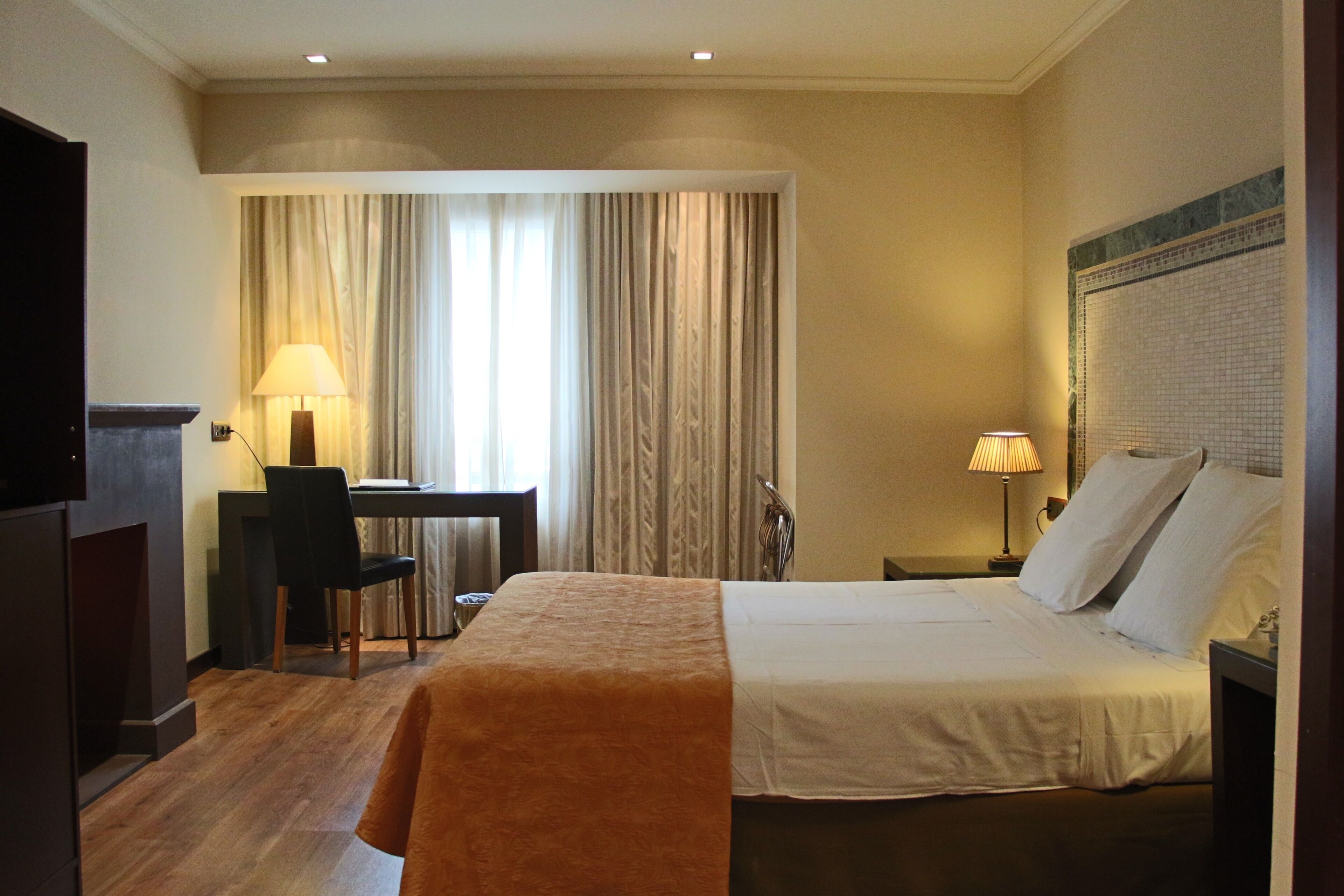 A hotel room with a bed, desk, chair, and two lamps.