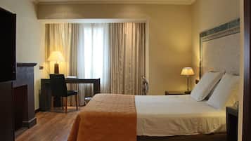 Una habitación de hotel con cama, escritorio, silla y dos lámparas.