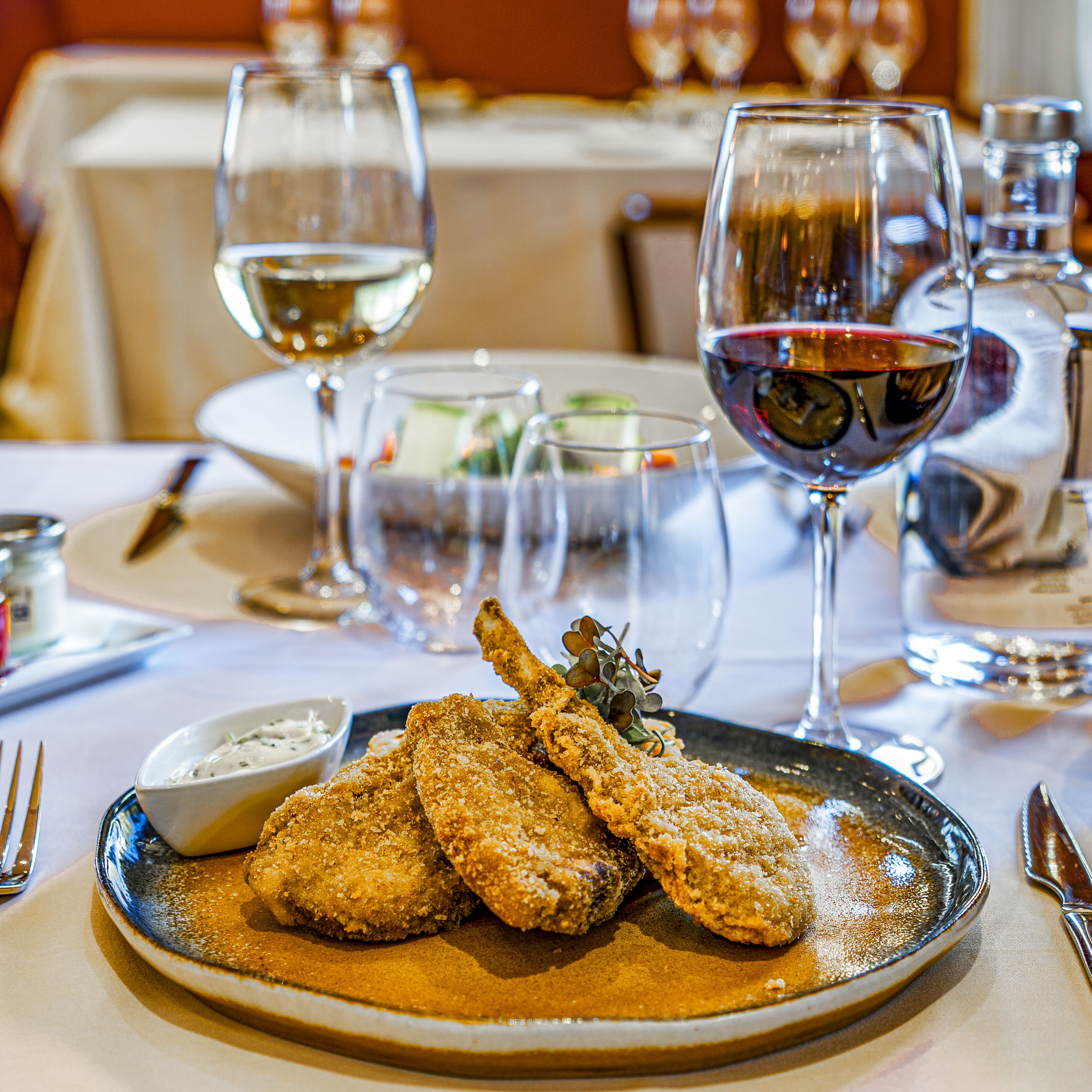 A dining table with a plate of breaded fish, wine glasses, and cutlery.