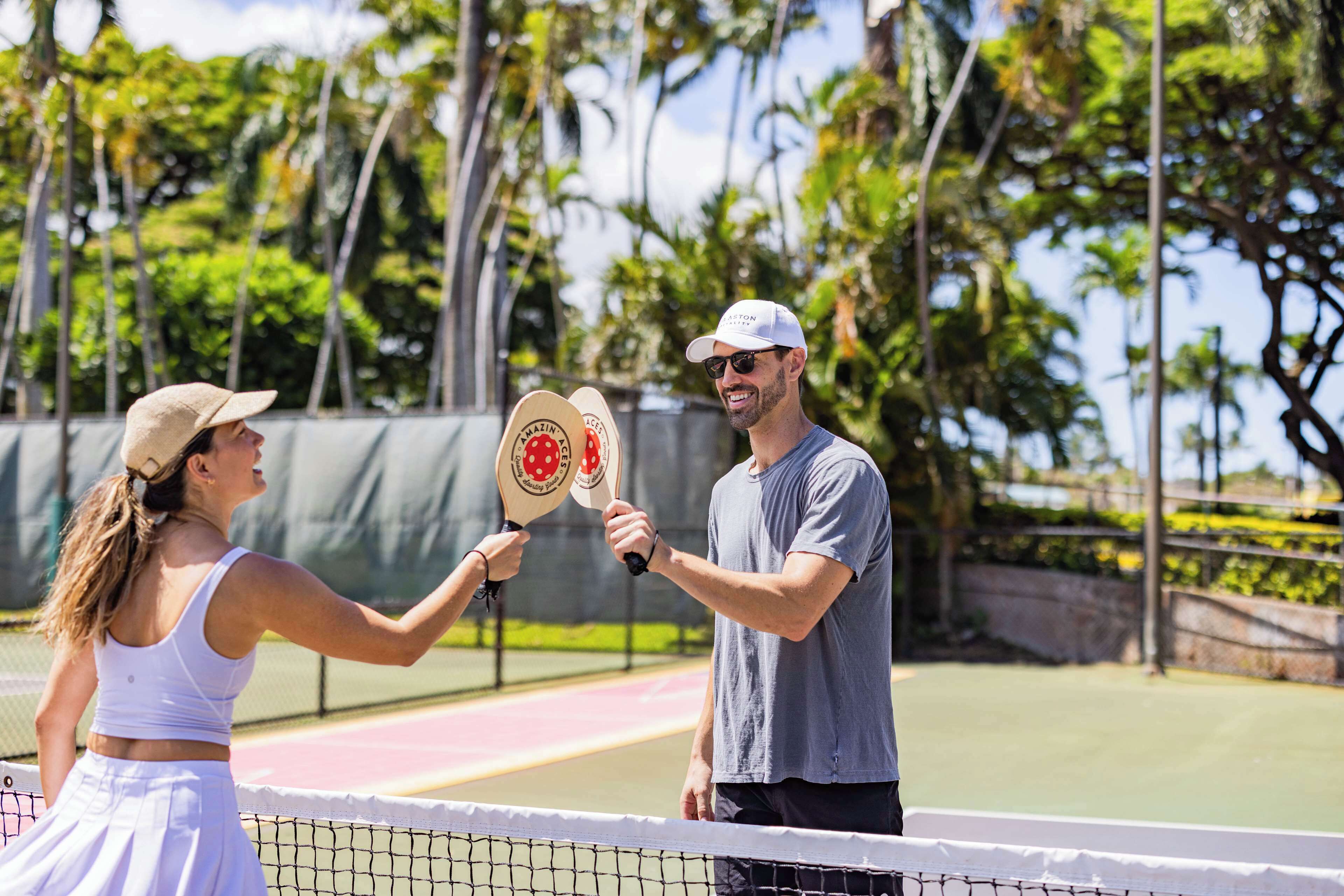 A tennis court with a net in the middle, surrounded by palm trees and a clear sky.