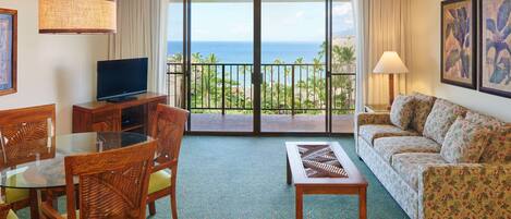 Ein Hotelzimmer mit Balkon, Fernseher, einer Couch und einem Essbereich mit Stühlen und Tisch.