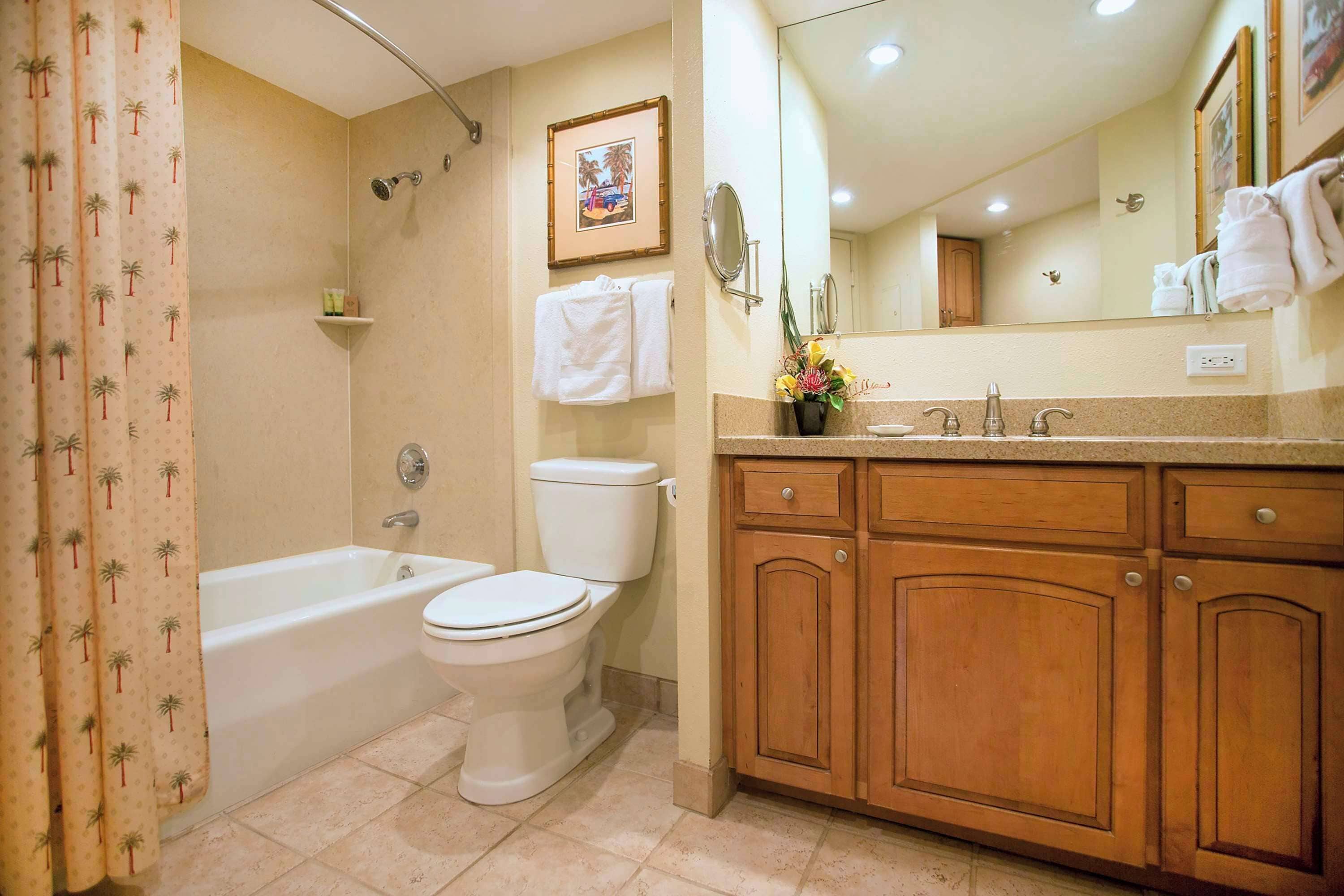 A bathroom with a bathtub, toilet, and vanity with wooden cabinets.