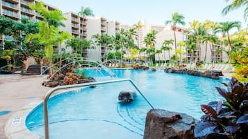 Una piscina con una formación rocosa, rodeada de palmeras y un edificio de varios pisos.
