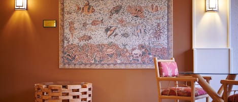 Une pièce décorée d’une mosaïque murale, avec une petite table en bois et un fauteuil en osier.