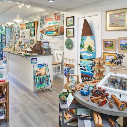 A well-lit art gallery with various paintings and sculptures displayed on shelves and tables.