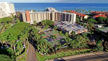 A hotel with a large parking lot, surrounded by palm trees and a view of the ocean.