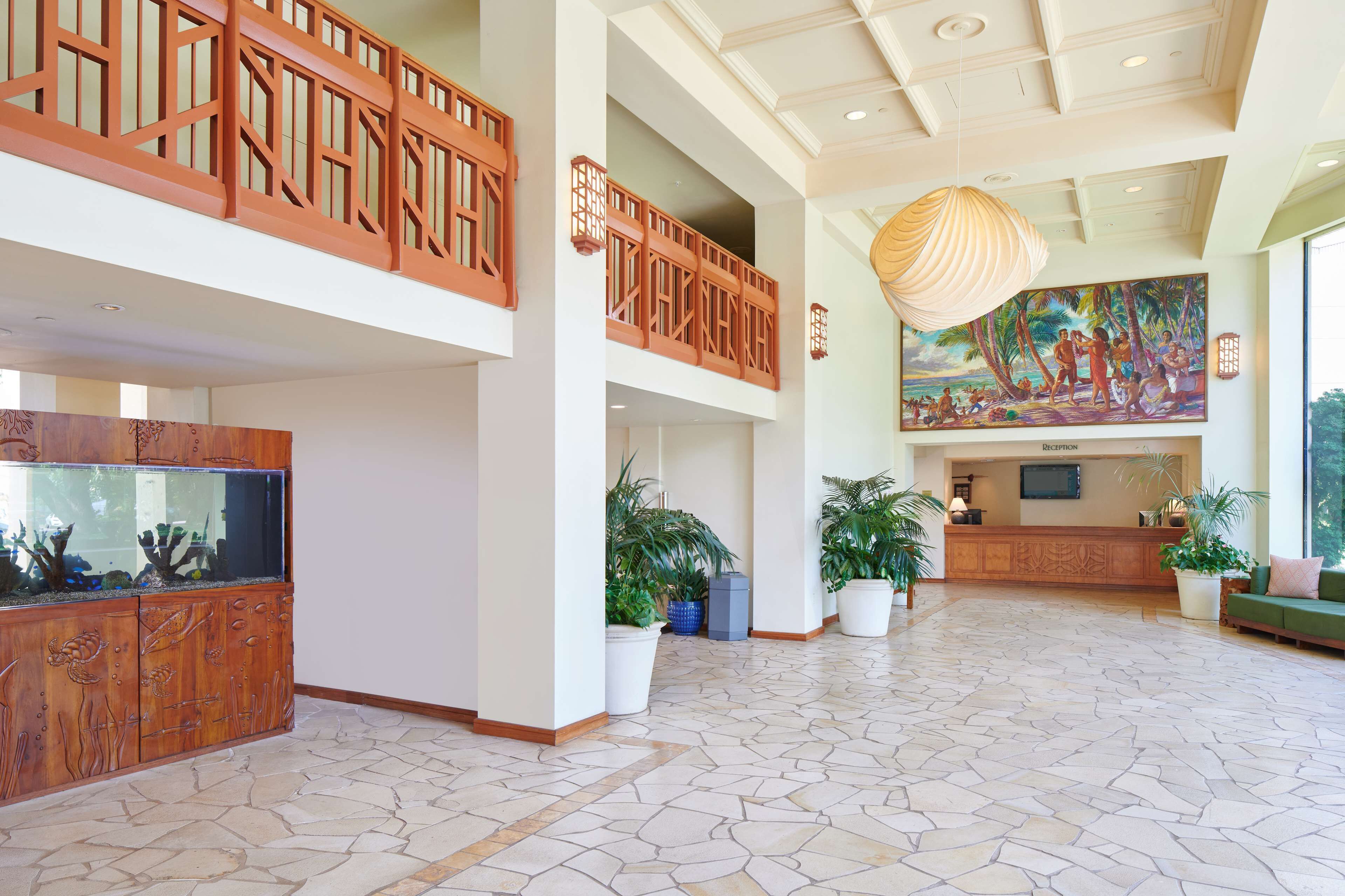 Un hall d’entrée spacieux avec un comptoir de réception, un grand aquarium et un plafond haut orné d’un luminaire décoratif.