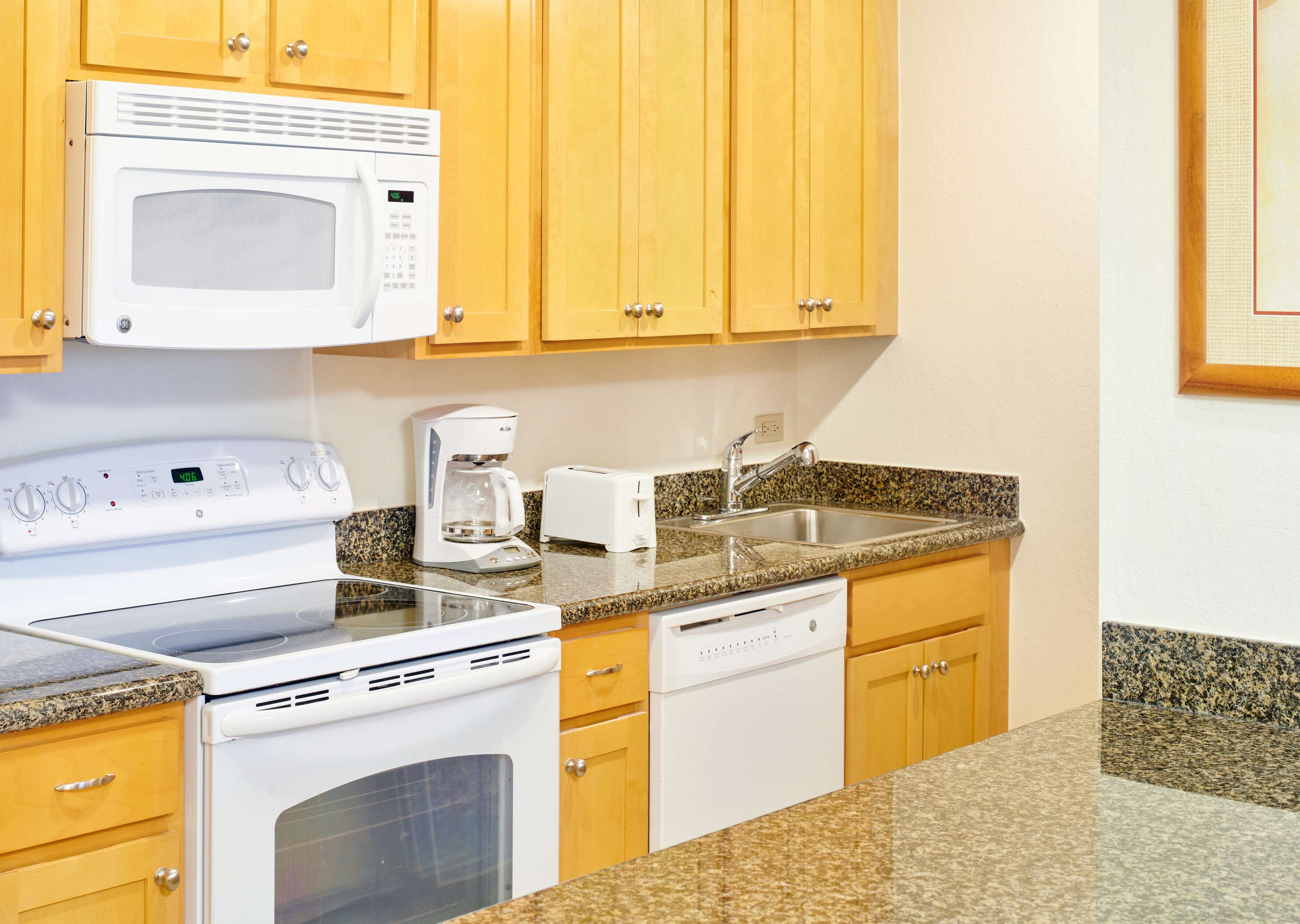 A kitchen with wooden cabinets, a microwave, a stove, a coffee maker, a toaster, and a dishwasher.