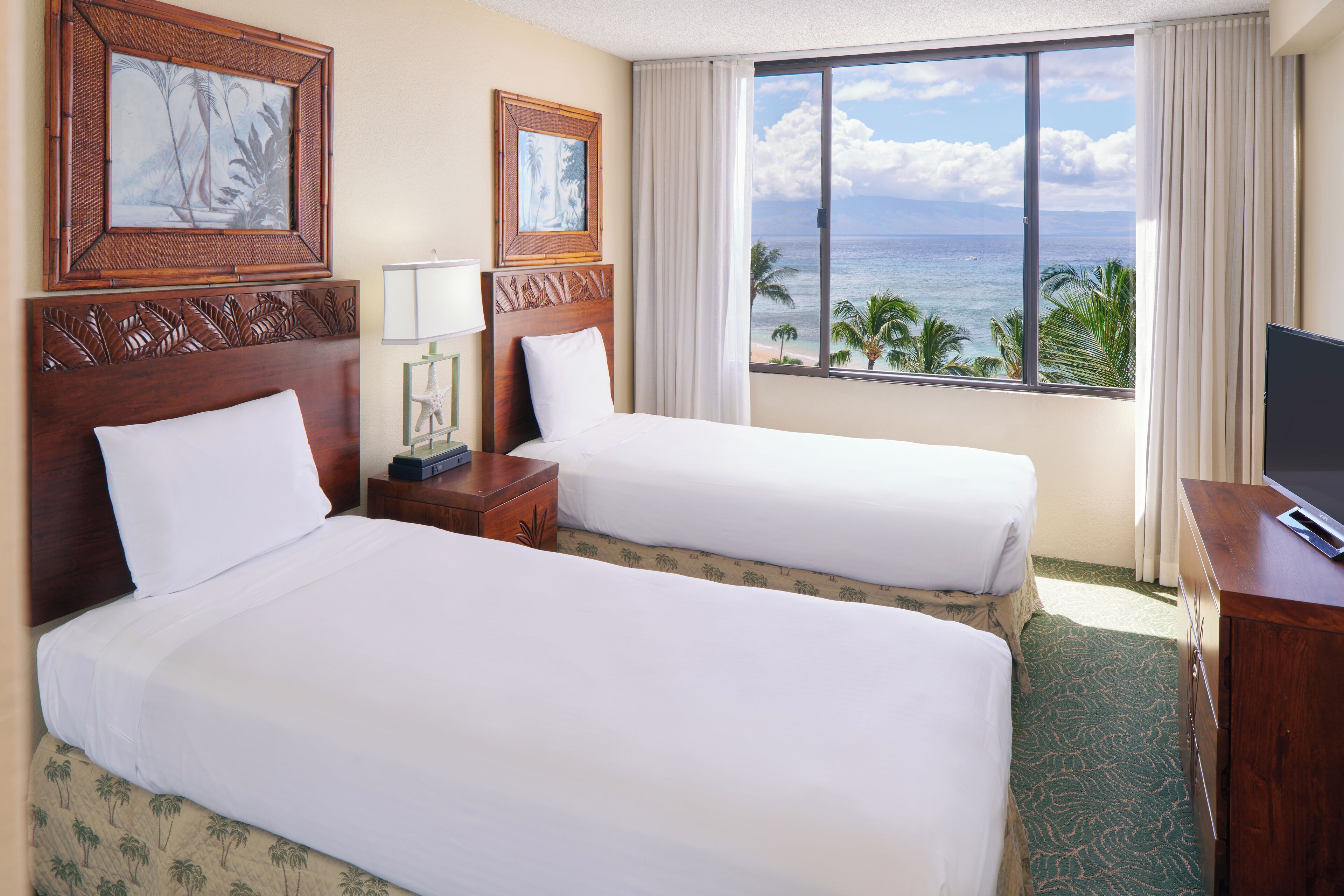 A hotel room with two beds, a large window with a view of the ocean, and a television on a wooden dresser.