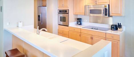 A modern kitchen with a central island, stainless steel appliances, wooden cabinets, and a coffee maker.