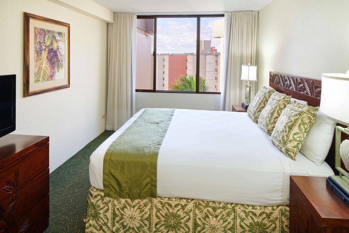 A hotel room with a large bed, a television, a window with curtains, and a framed picture on the wall.