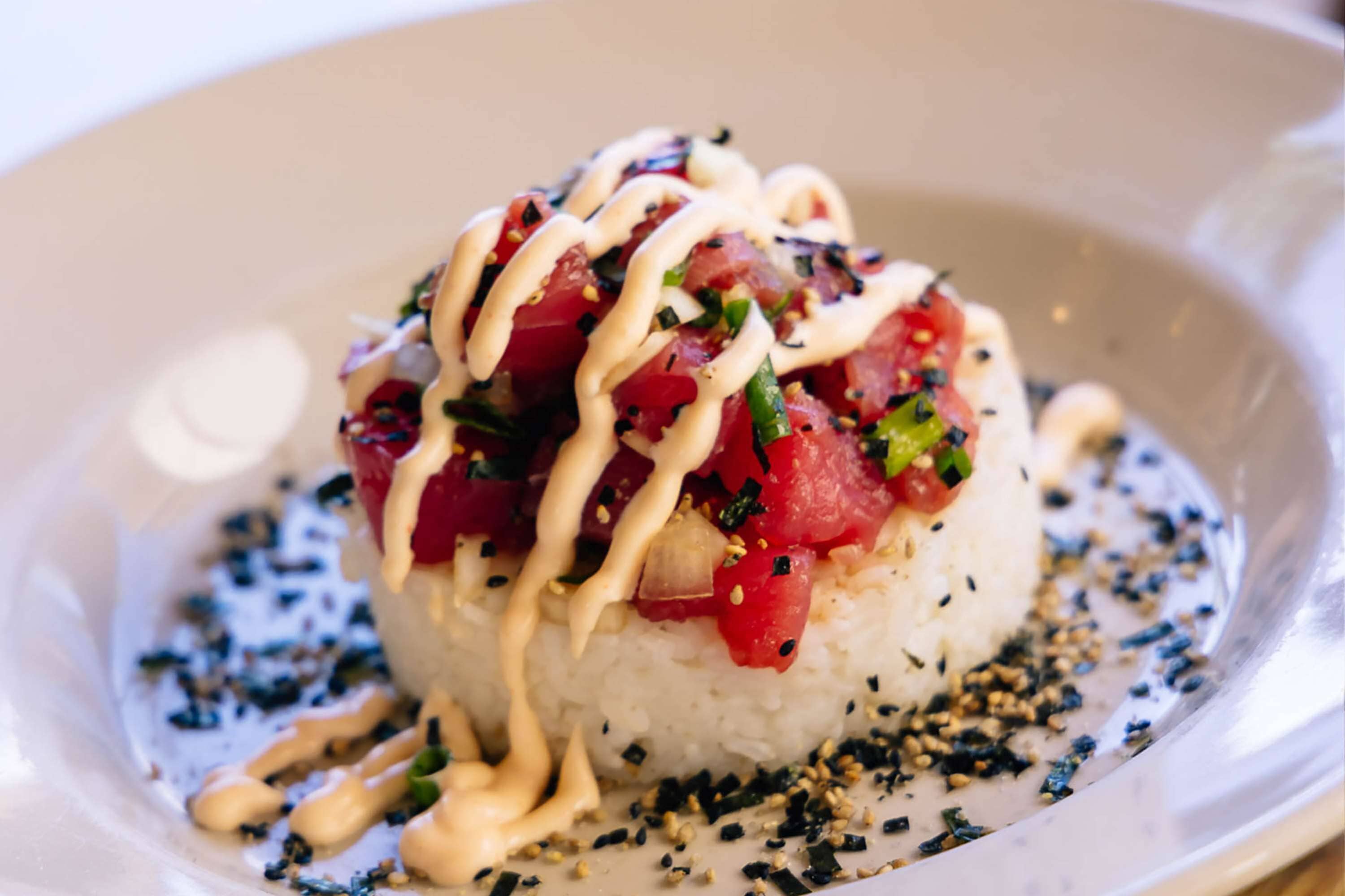 A dish with rice, diced red ingredients, green herbs, and a creamy sauce on a plate.