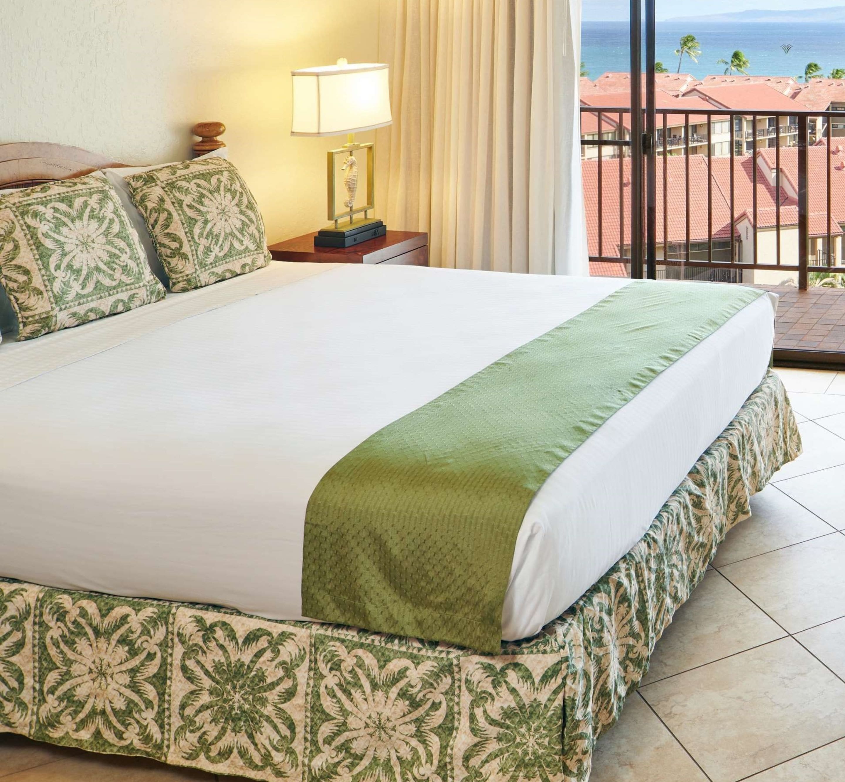 A hotel room with a large bed, a nightstand with a lamp, and a view of the ocean through a balcony.