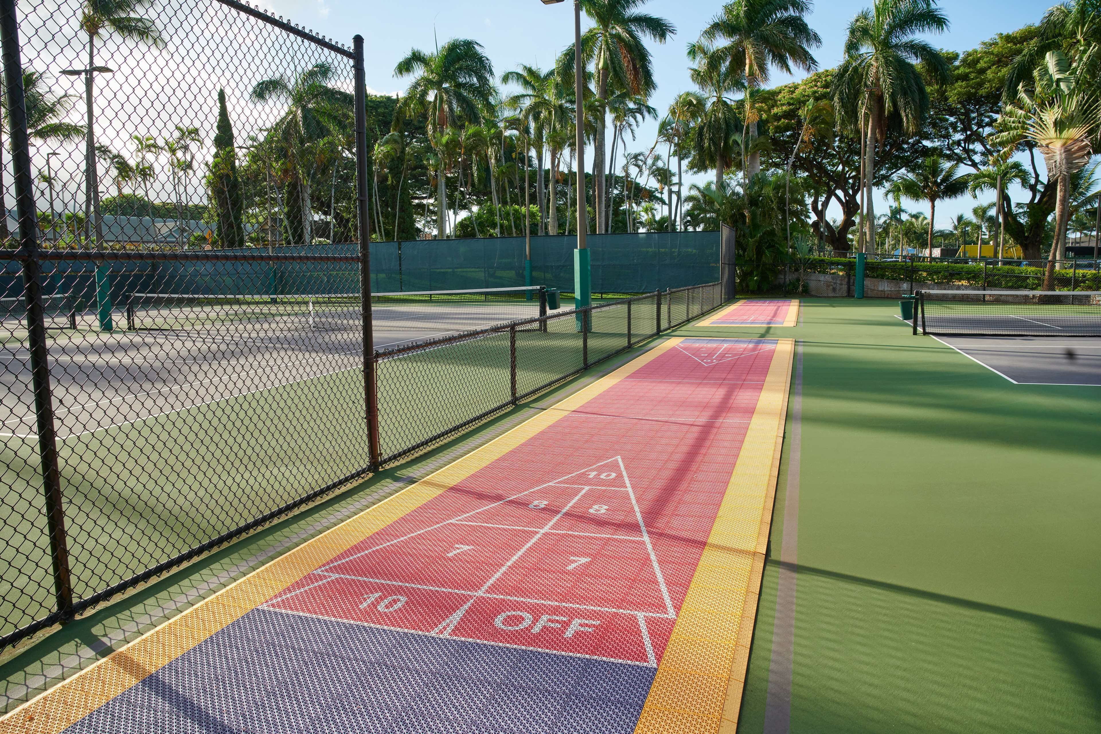 A tennis court with a green surface, a net, and a hopscotch game area.