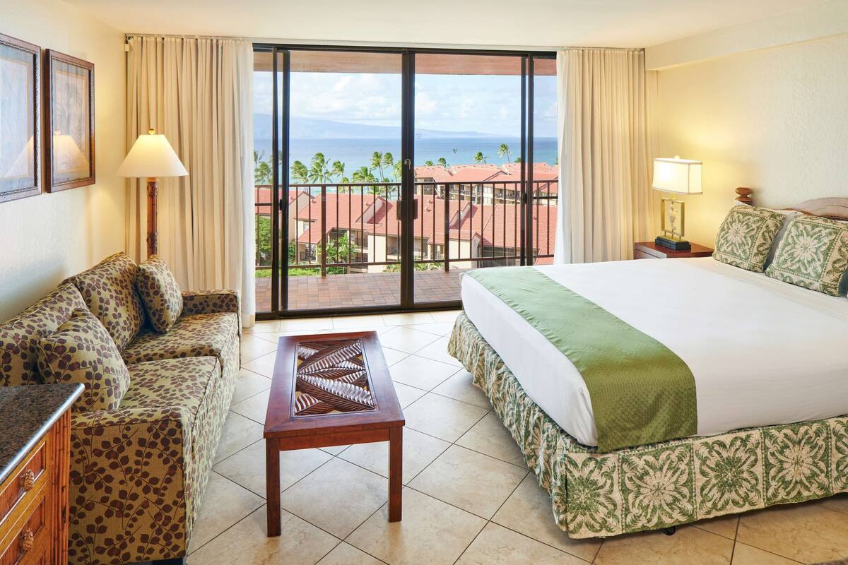 A hotel room with a bed, a sofa, a table, and a view of the ocean.