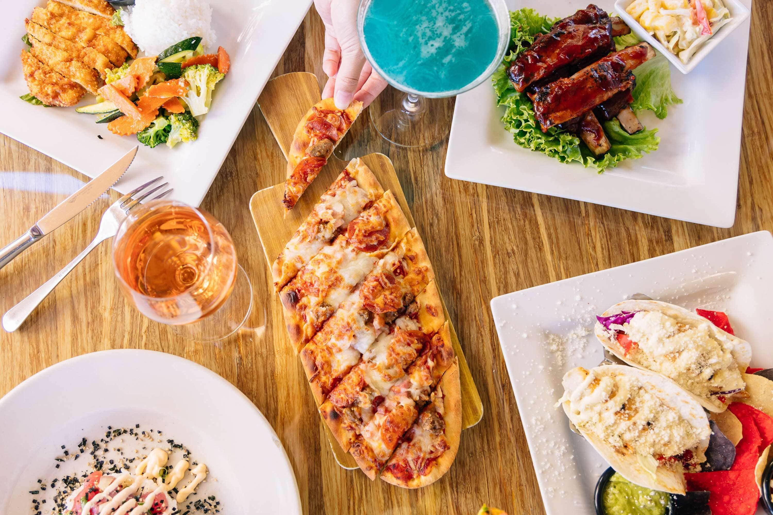 A variety of dishes including pizza, ribs, and tacos on a wooden table.