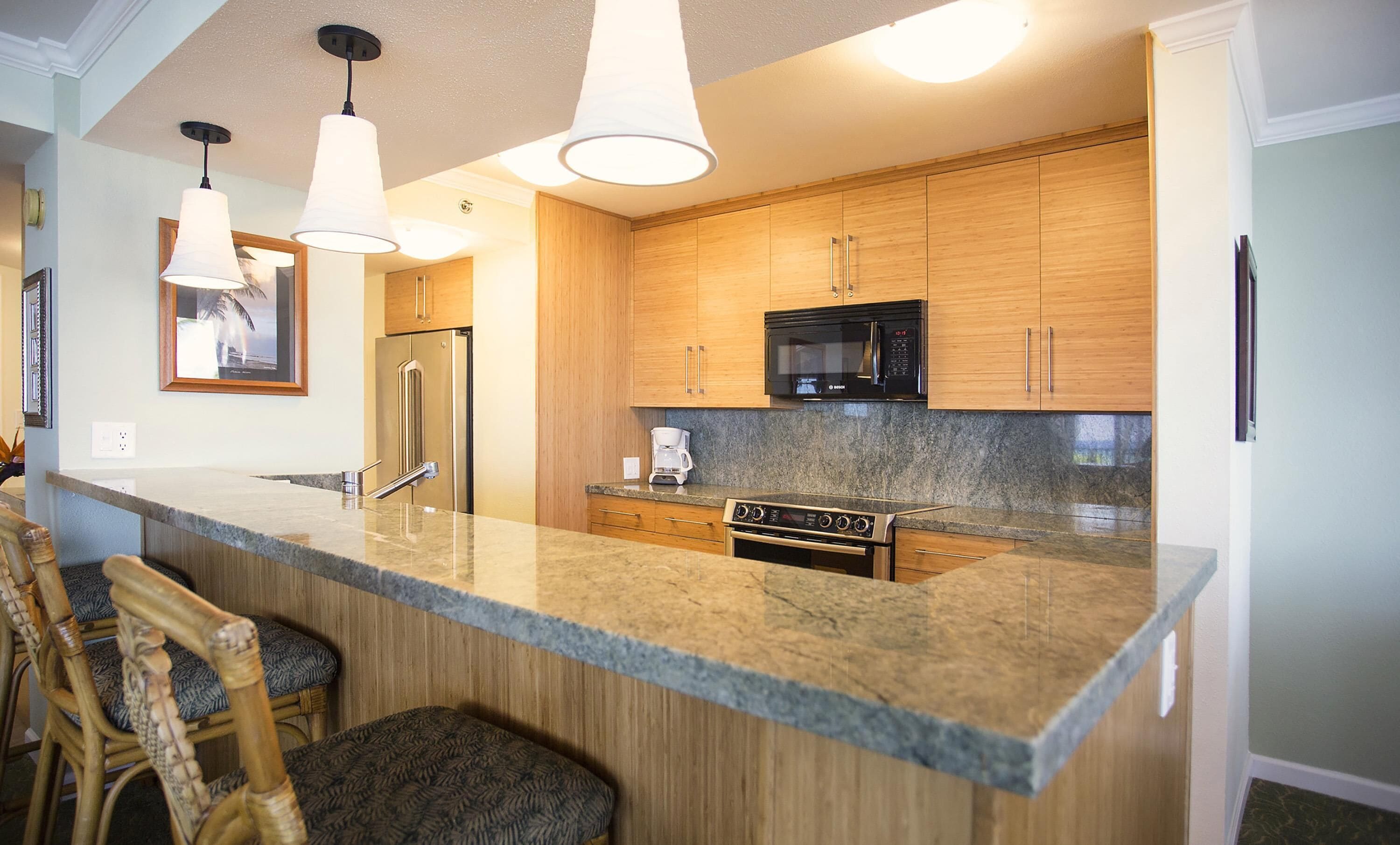 A modern kitchen with wooden cabinets, a built-in microwave, a stainless steel refrigerator, and a granite countertop.