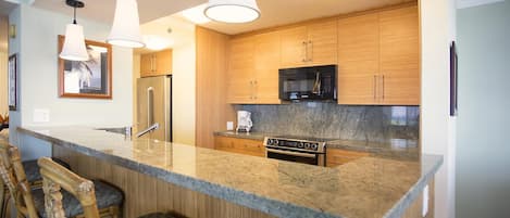 Una cocina moderna con armarios de madera, microondas integrado, refrigerador de acero inoxidable y encimera de granito.