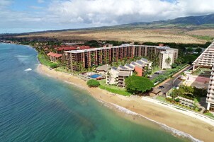 A coastal resort with beachfront villas, a pool, and a view of the ocean and hills.