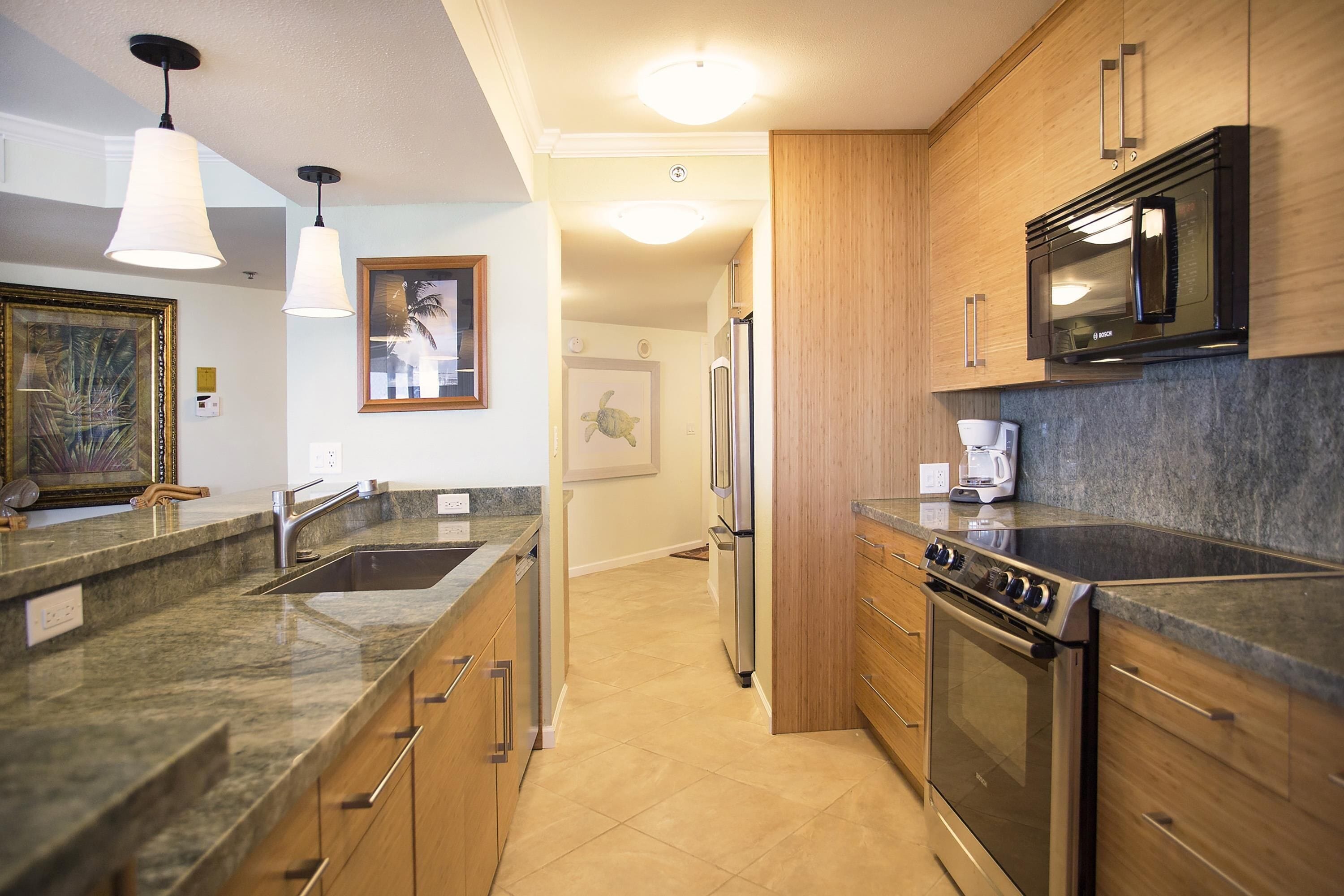 A modern kitchen with granite countertops, stainless steel appliances, wooden cabinets, and pendant lighting.