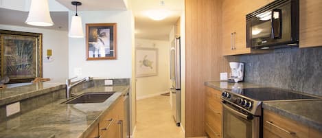 A modern kitchen with granite countertops, stainless steel appliances, wooden cabinets, and pendant lighting.