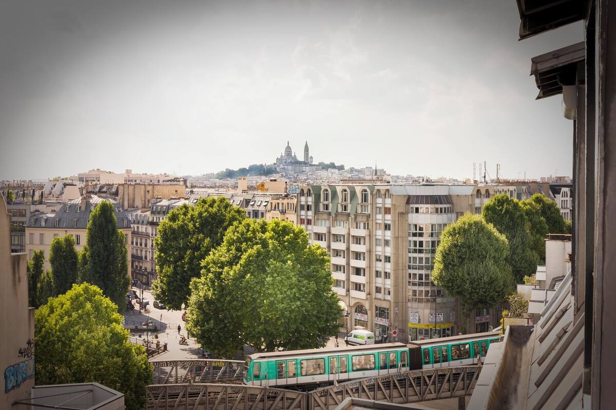 A cityscape with a prominent building in the background, a green tram in the foreground, and a mix of residential and commercial buildings.