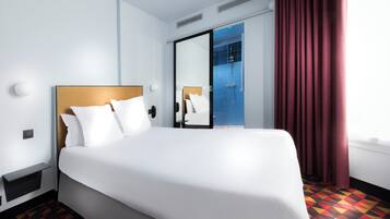Habitación de hotel con una cama grande, una mesita de noche, un espejo, zona de ducha y una cortina roja.