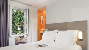 A hotel room with a bed, a window with curtains, a bedside table with a handbag, and a wall-mounted phone. - Libertel Canal Saint Martin (Paris)