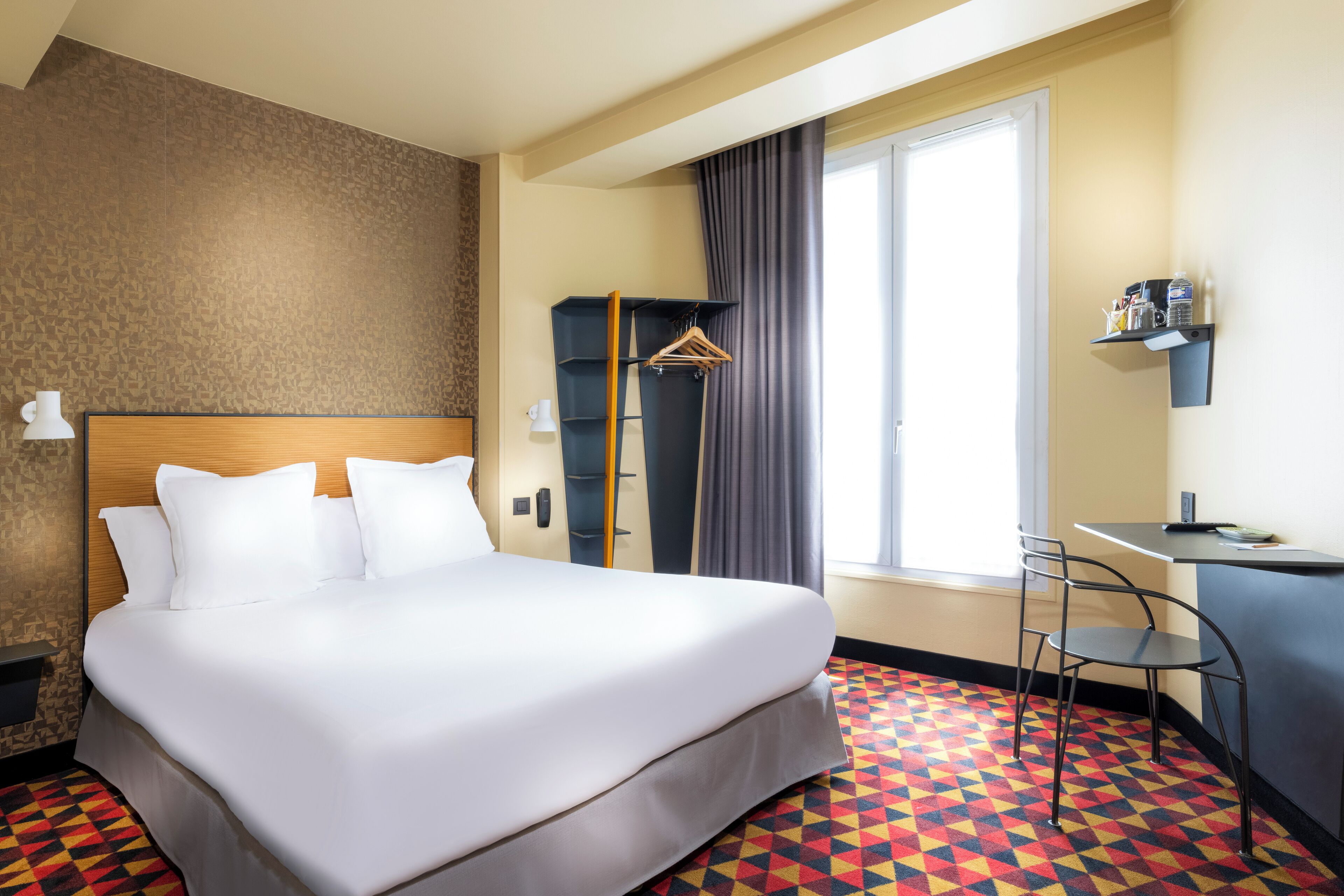 A hotel room with a large bed, a desk, a chair, a wardrobe, and a window with curtains.