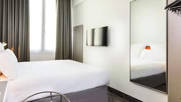 Quarto de hotel com uma cama, televisão de tela plana, espelho grande e janela com cortinas.