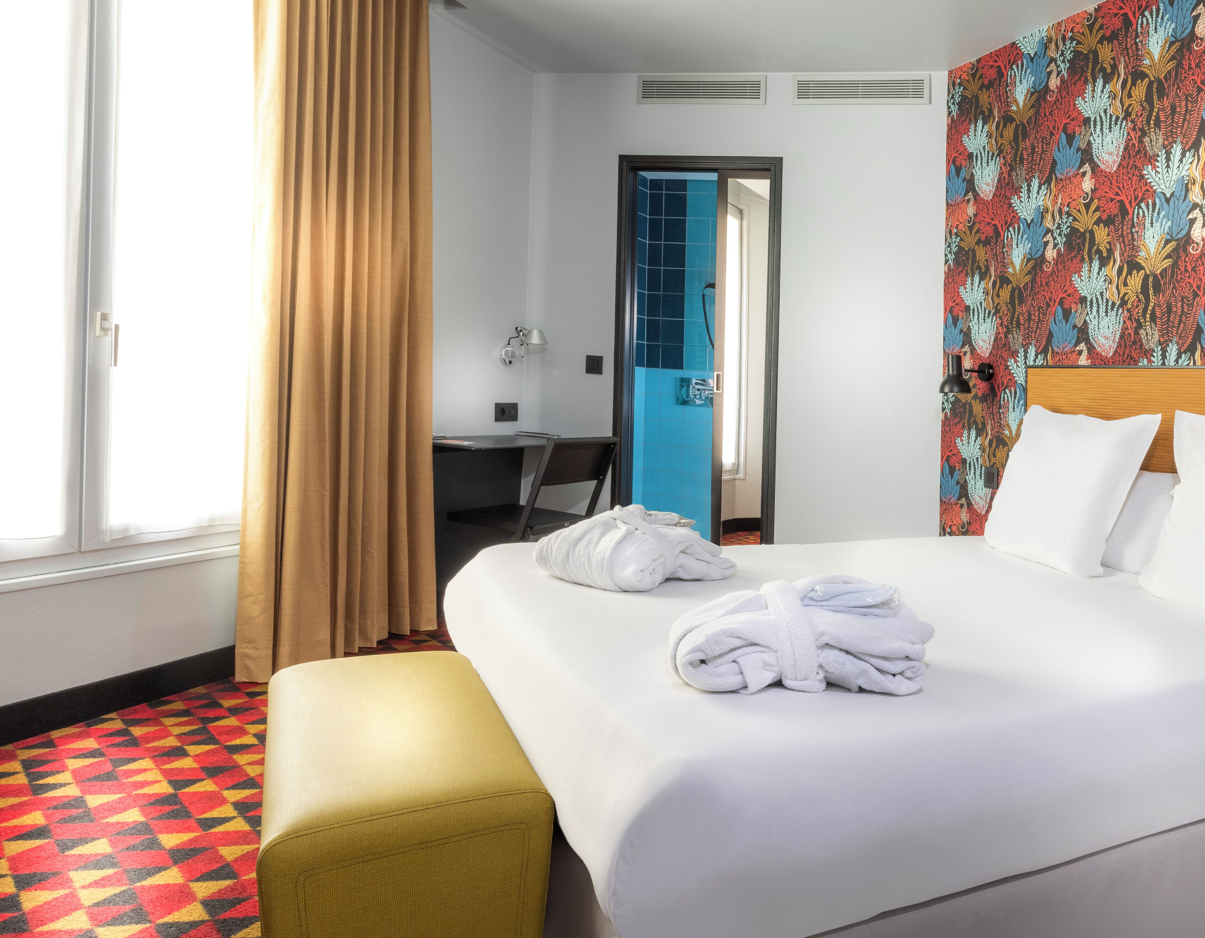 Une chambre d’hôtel avec un lit, un bureau, une chaise et une fenêtre avec des rideaux.