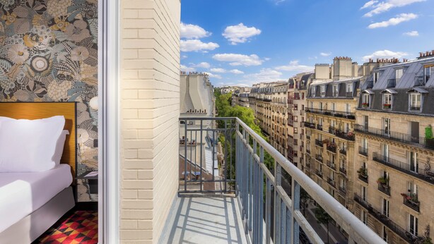 A balcony with a bed, a patterned wall, and a view of Parisian buildings. - Libertel Canal Saint Martin (Paris)