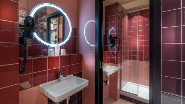Een badkamer met rode tegels, een wit wastafelmeubel, een spiegel met verlichting en een douche.
