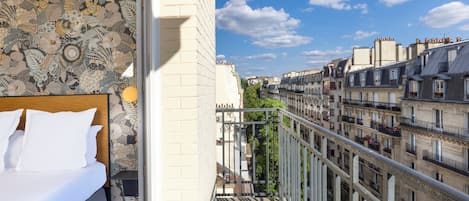A hotel room with a bed, a patterned wall, and a balcony overlooking a cityscape.