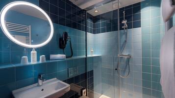 Uma casa de banho moderna com cabine de duche em vidro, lavatório branco e espelho com iluminação circular.