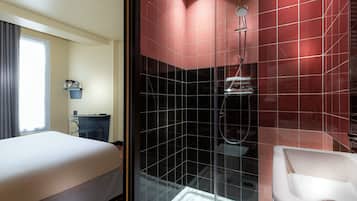 A hotel room with a bed, a desk, a shower with red tiles, and a sink.