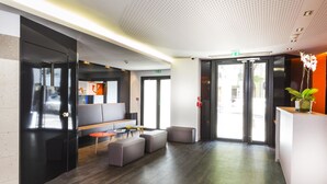A modern lobby with a reception desk, seating area, and a large glass door leading outside. - Libertel Canal Saint Martin (Paris)