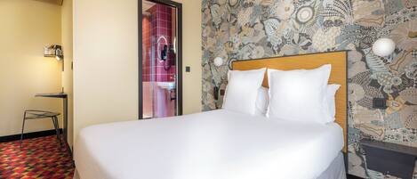 Quarto de hotel com uma cama grande, uma mesinha pequena e parede estampada.