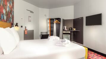 Habitación de hotel con cama, mesita de noche, armario, televisor y pequeña cocina.