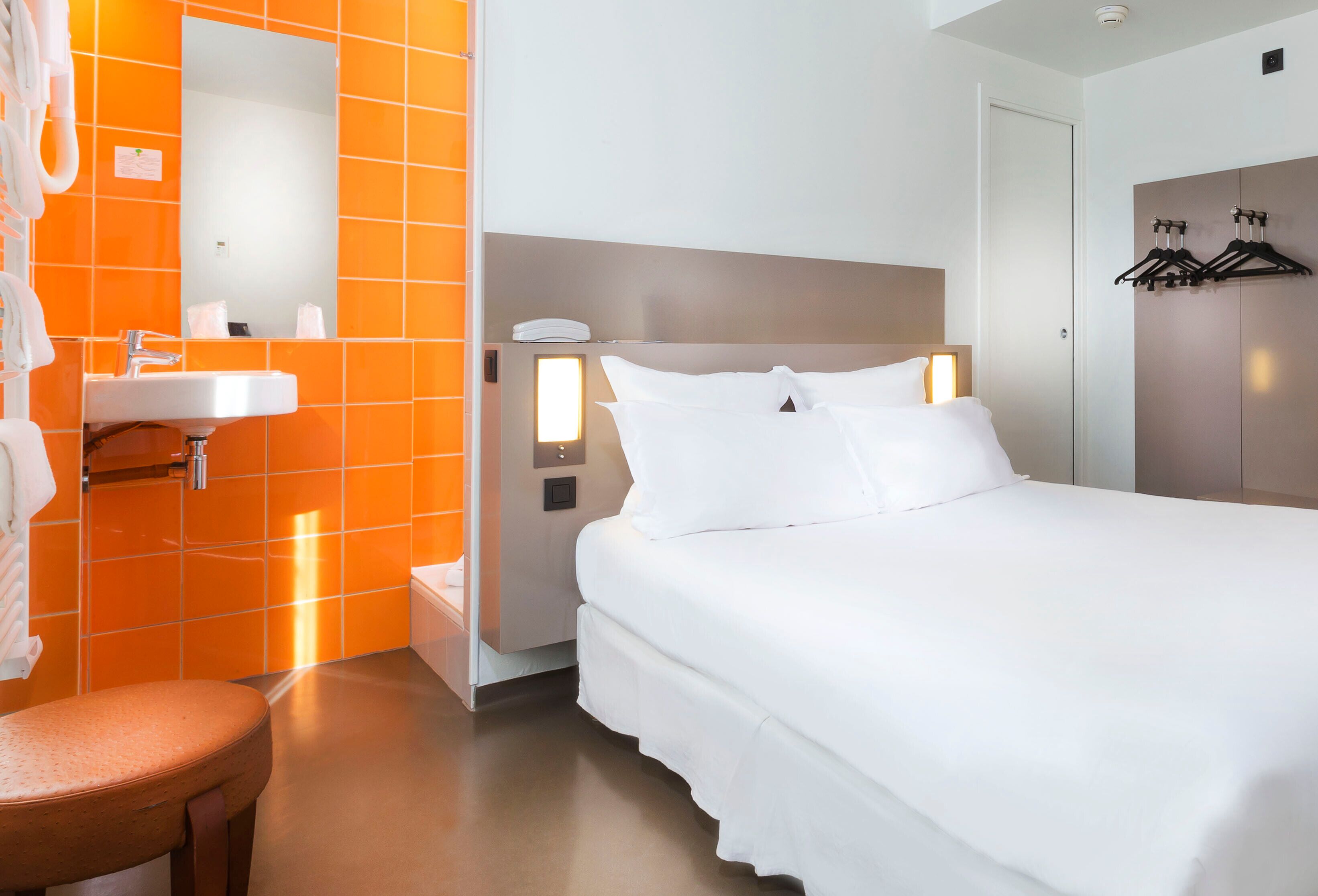 A hotel room with a white bed, a white sink, and orange-tiled walls.