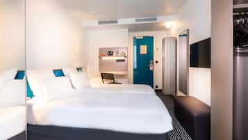A hotel room with a large bed, a desk, a chair, a wardrobe, a mirror, and a door.