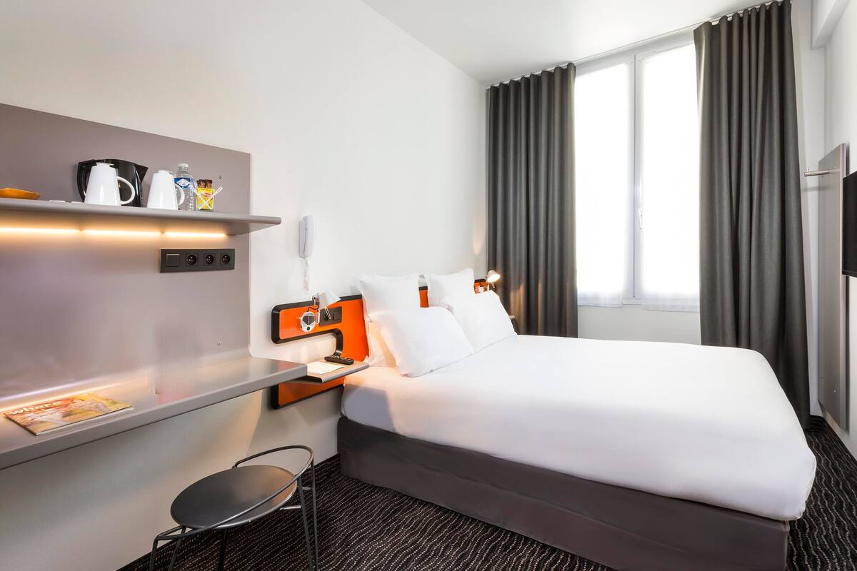 A hotel room with a bed, bedside table, lamp, and a small chair.