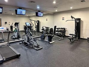 Ein Fitnessstudio mit Laufbändern, Krafttrainingsgeräten und einem Fernsehbildschirm.