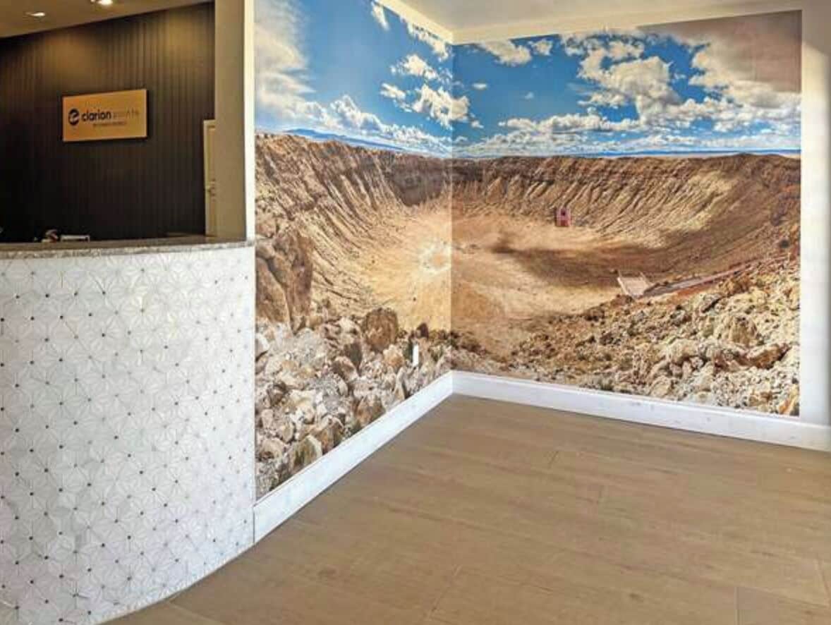 Un área de recepción con un mural panorámico de un cañón, una mesa de recepción y piso de madera.