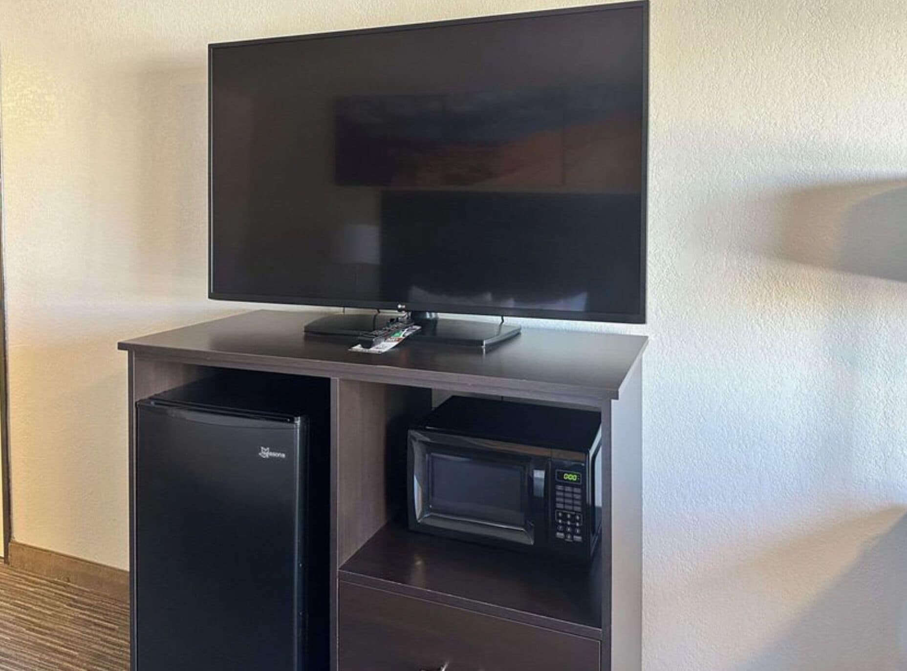 A flat-screen TV mounted on a cabinet with a refrigerator and a microwave below.