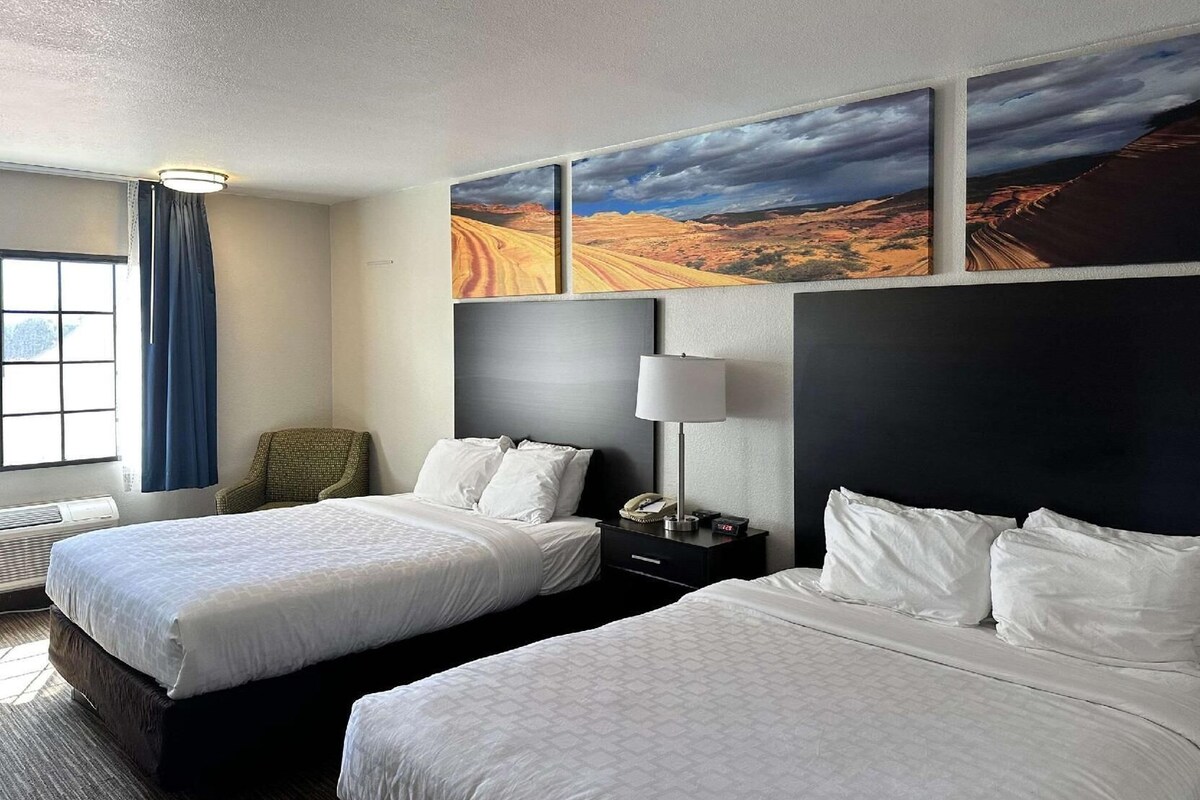 Une chambre d’hôtel avec deux lits, un bureau avec une lampe, une chaise et des œuvres d’art accrochées aux murs.